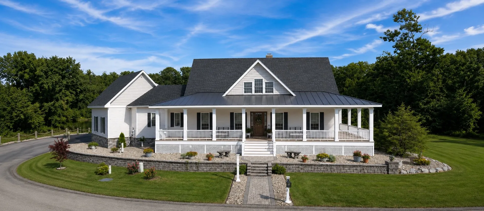 White farmhouse with a wraparound porch on a curved stone drive