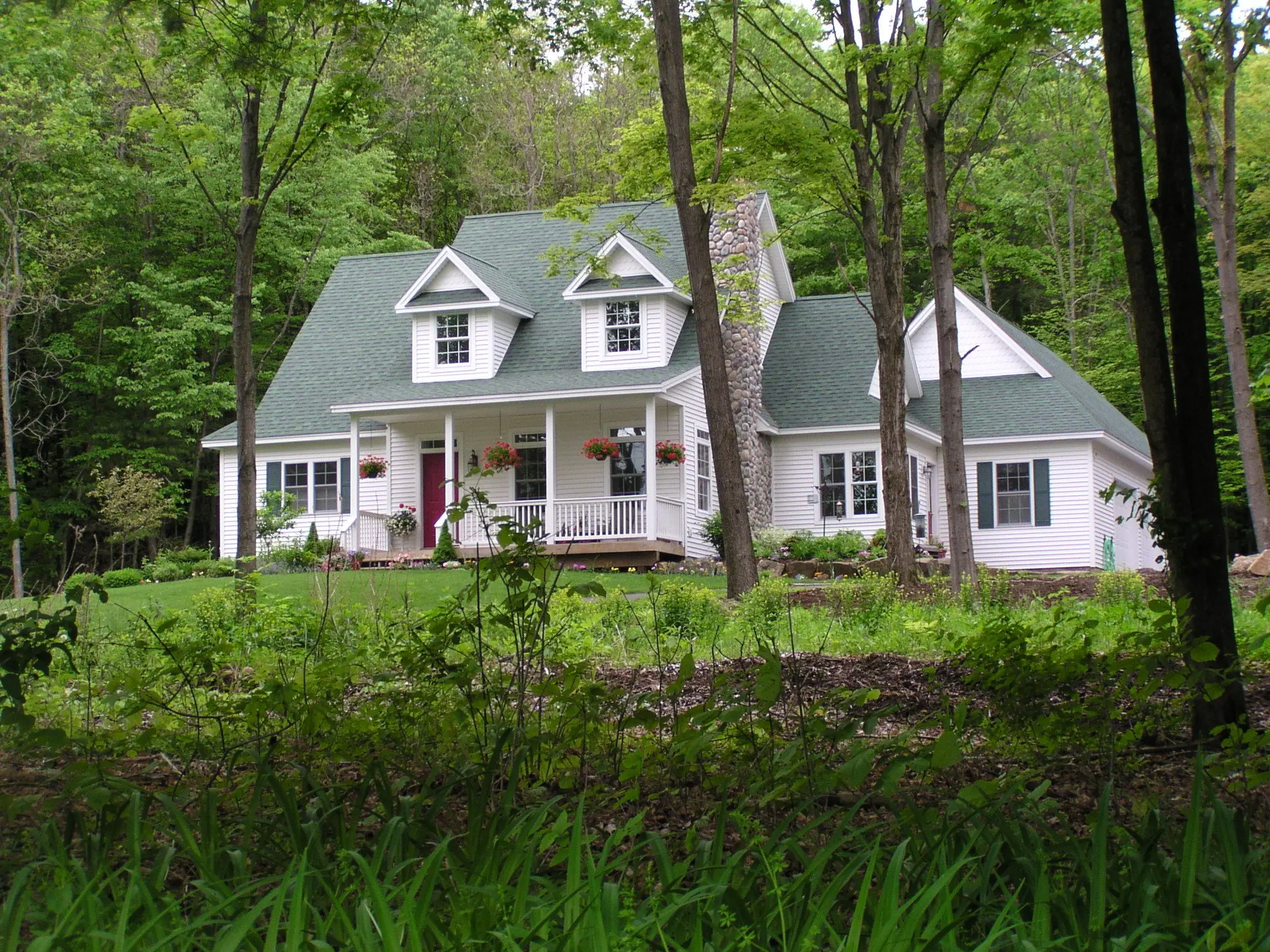 White Cape with dormers and a green roof among tall trees