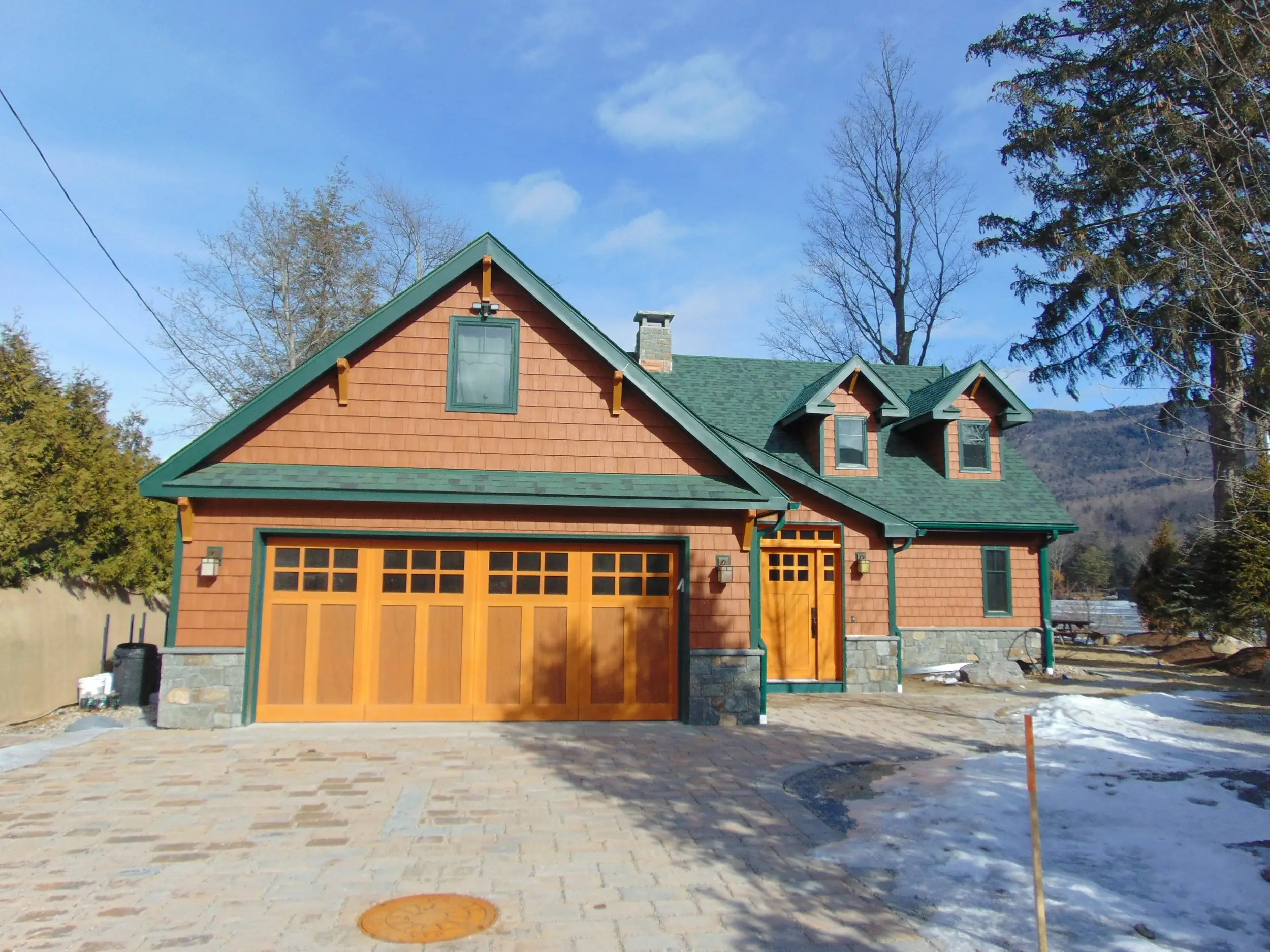 Cedar-shingled garage with wood carriage doors and a green roof, mountains behind