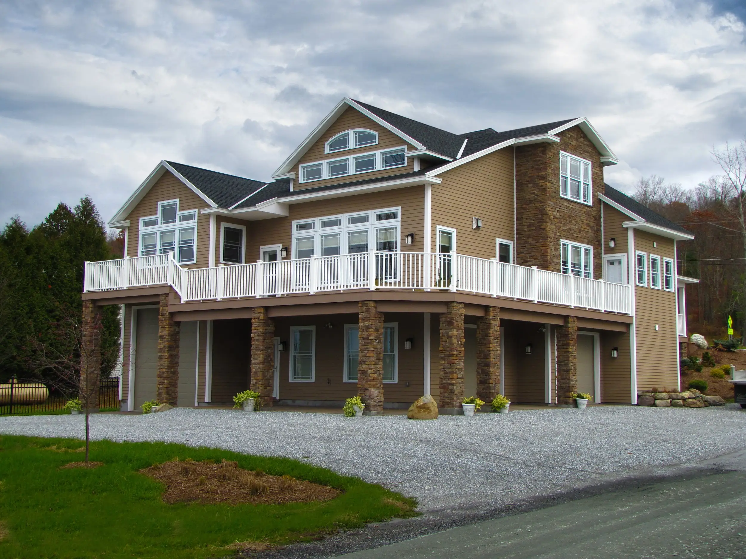 Tan-sided home with a white-railed wraparound deck on stone columns